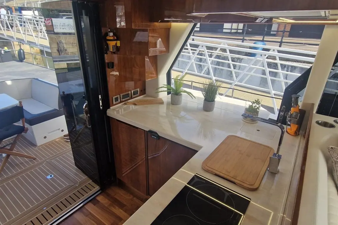 Bright modern kitchen on a boat featuring a marble countertop, potted plants, induction hob, and large window overlooking the dock.